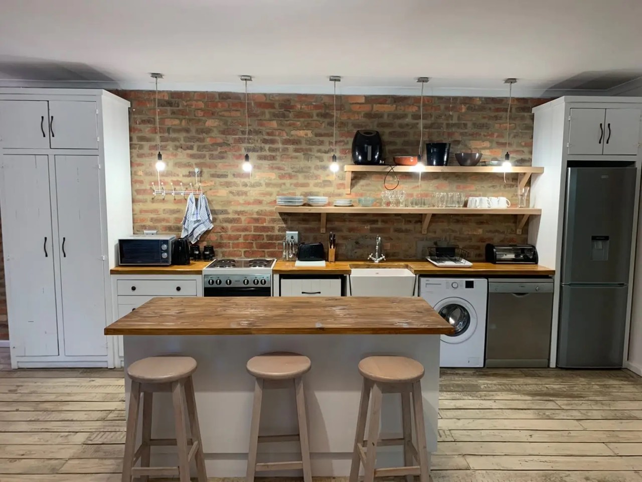 Kitchen with exposed brick wall, open shelving and island with bar stools